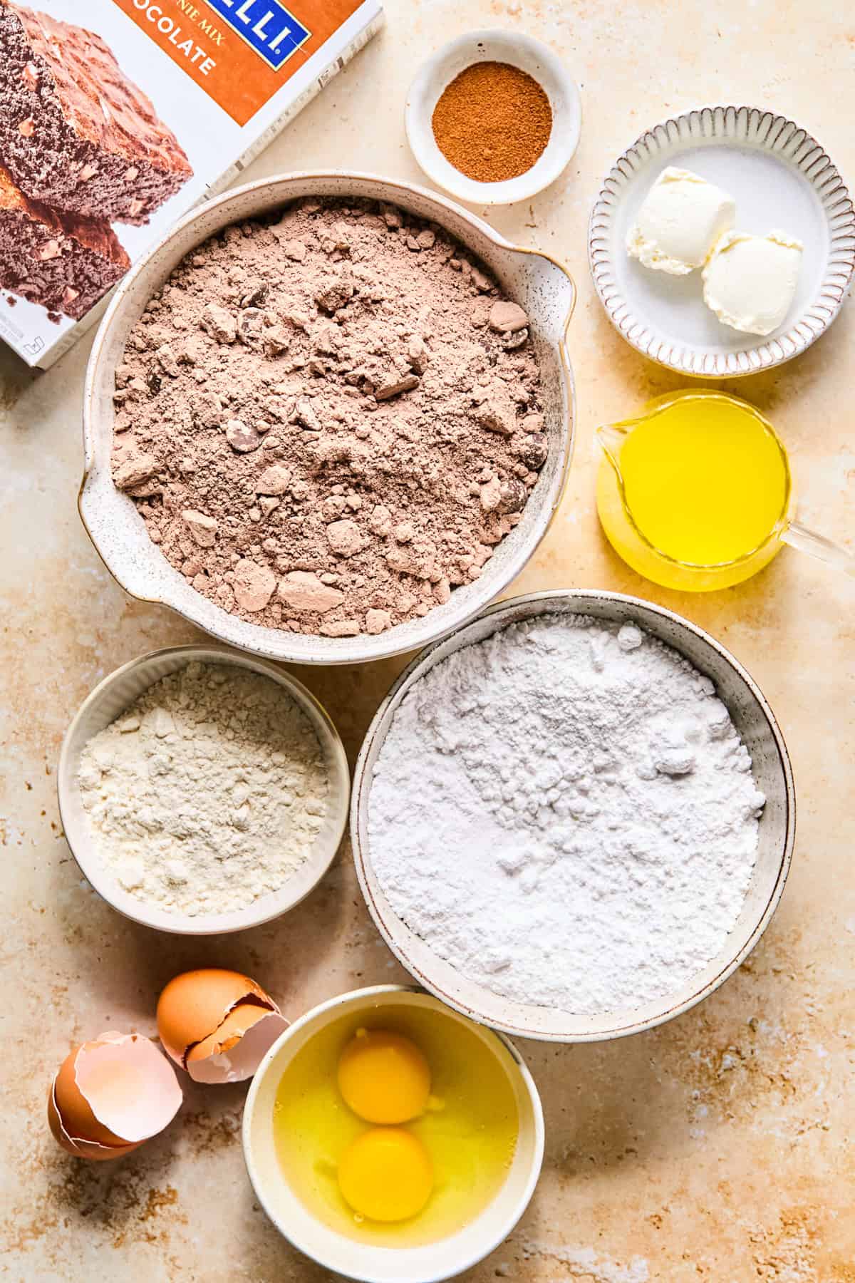 Brownie mix, powdered sugar, eggs and other ingredients arranged on surface.