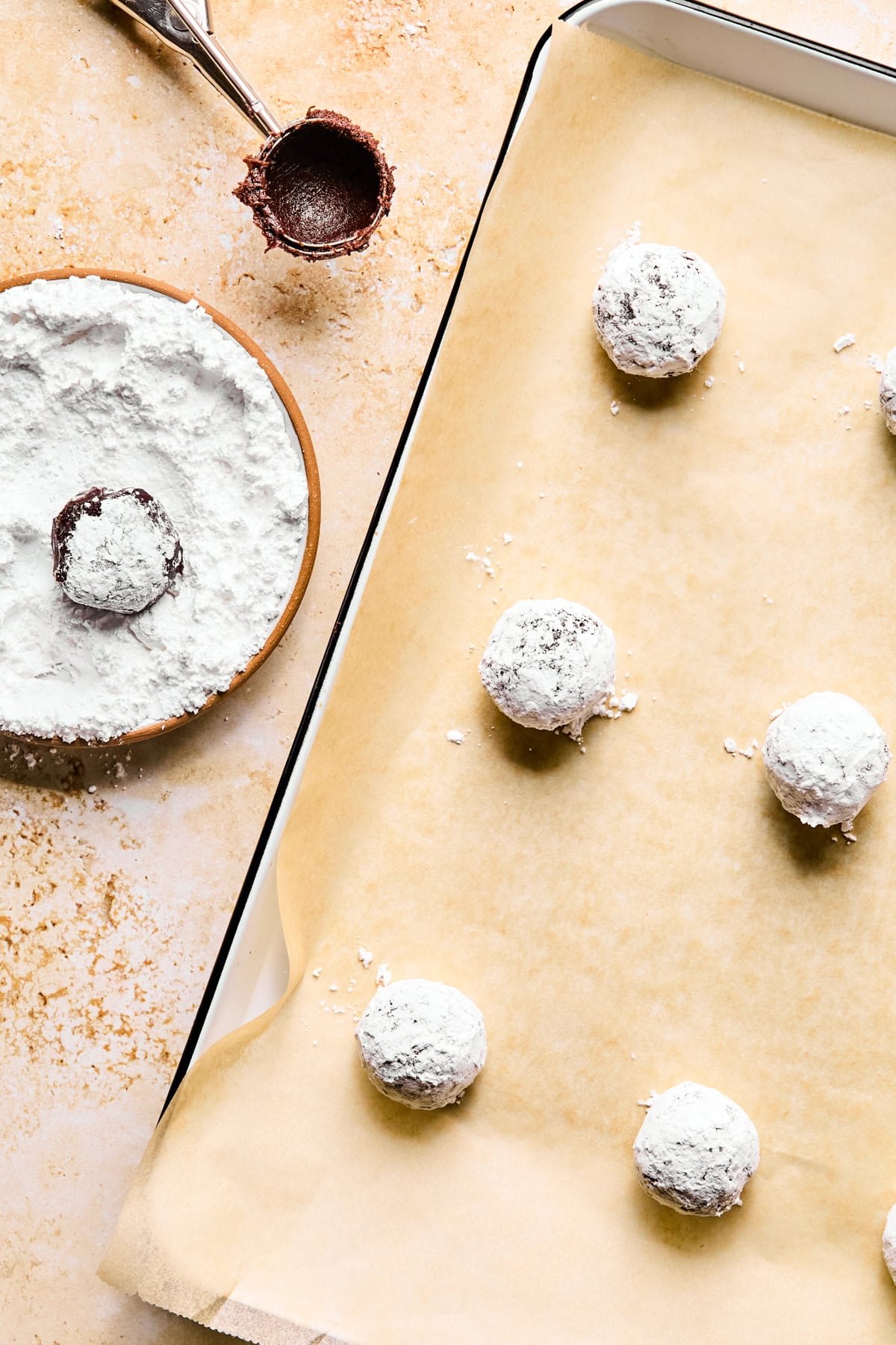 Parchment lined pan with chocolate crinkle cookie dough balls rolled in powdered sugar.