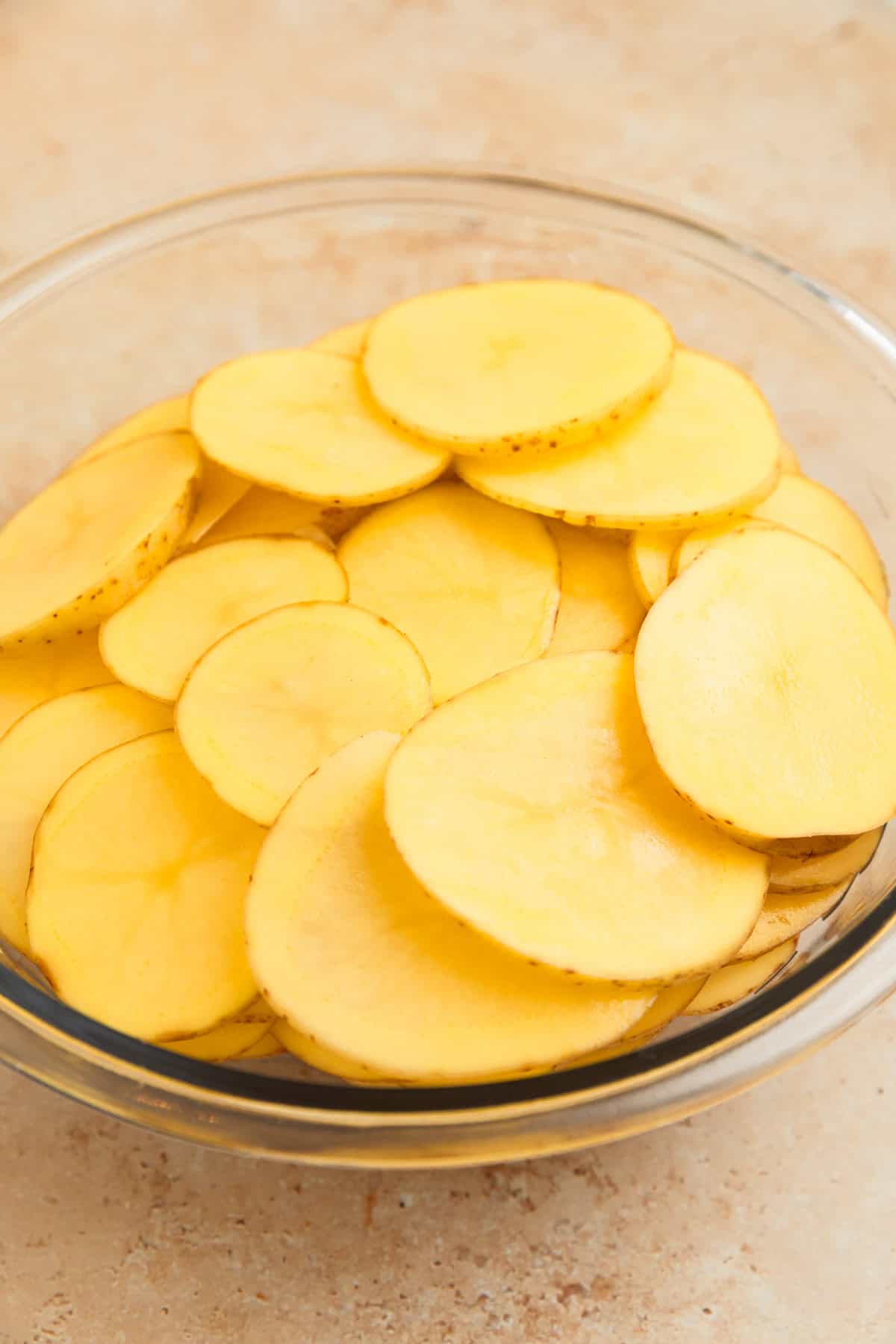 Sliced potatoes in glass mixing bowl.