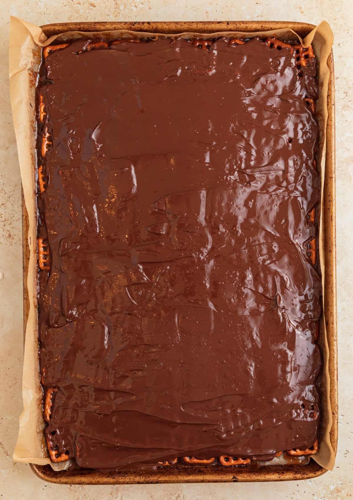 Melted chocolate chips spread over top of pretzel toffee.