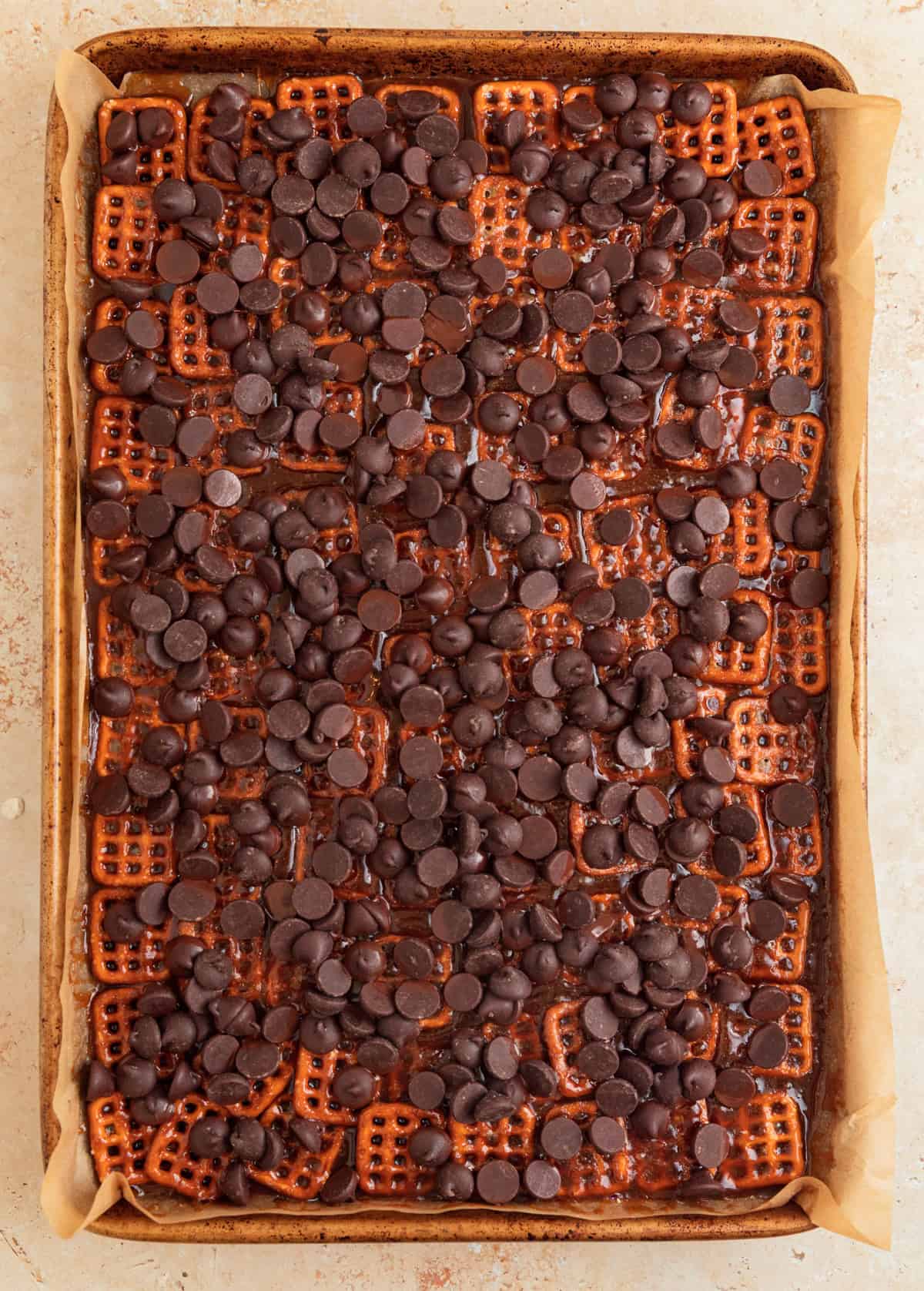 Chocolate chips sprinkled over top of pretzel toffee on sheet pan.