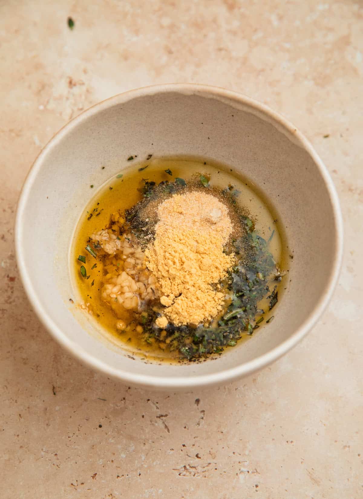 Seasoning and herbs added to bowl with olive oil.
