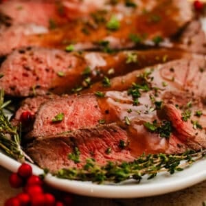 Sliced roast beef on plate with thyme and pomegranate.