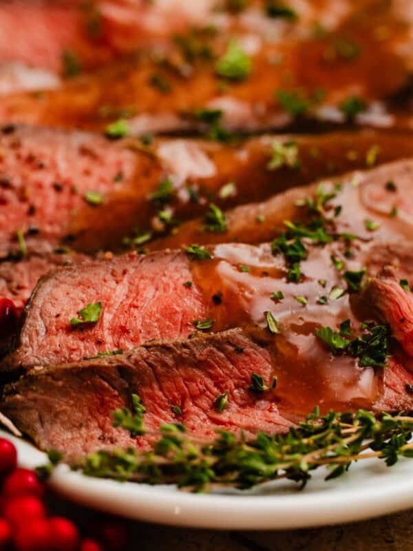 Sliced roast beef on plate with thyme and pomegranate.