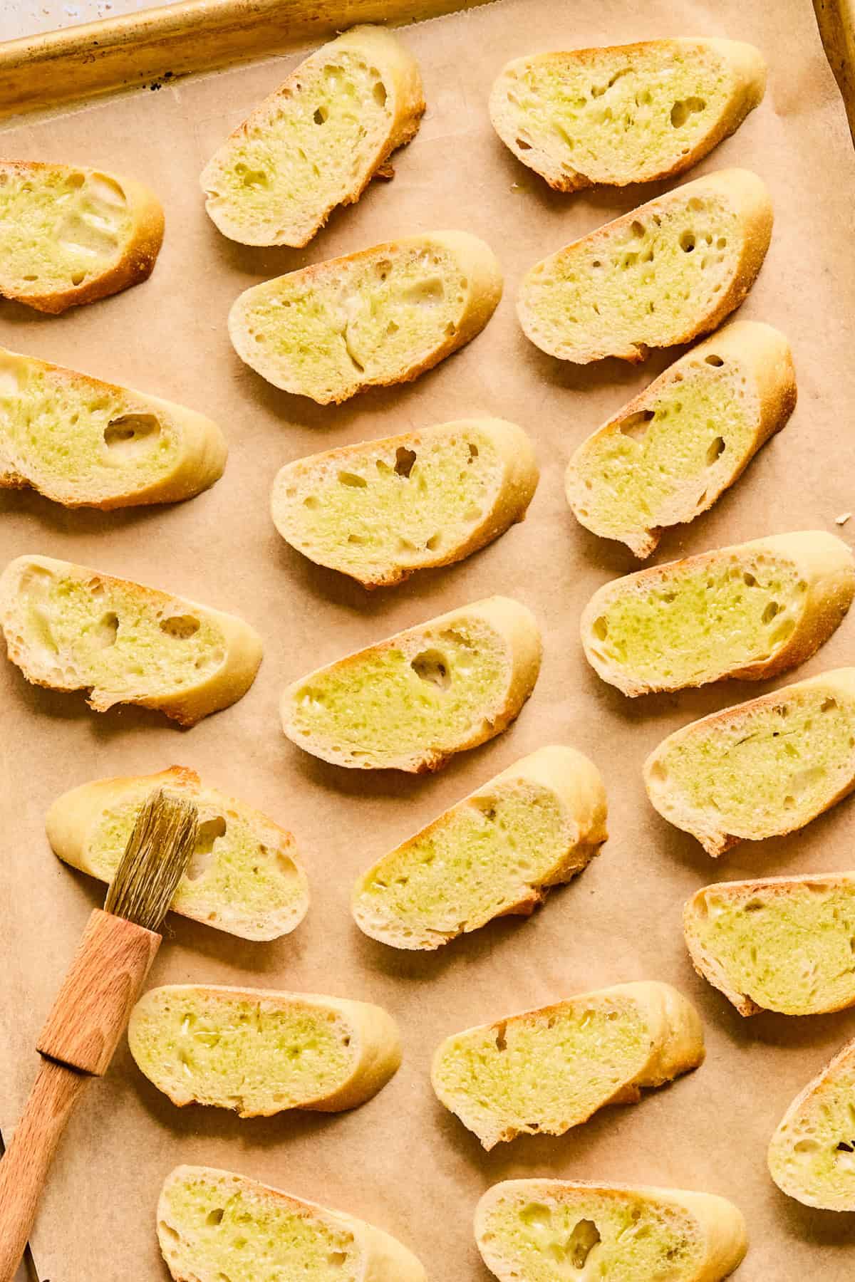 Sliced baguette on parchment lined pan with olive oil brushed over top.