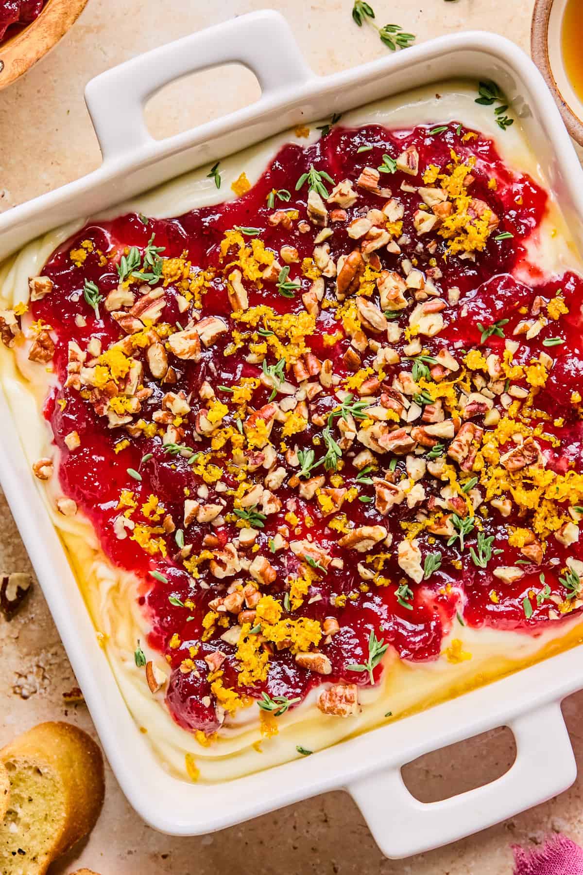 Ricotta dip in dish with cranberry sauce, pecans, thyme and orange zest over top.