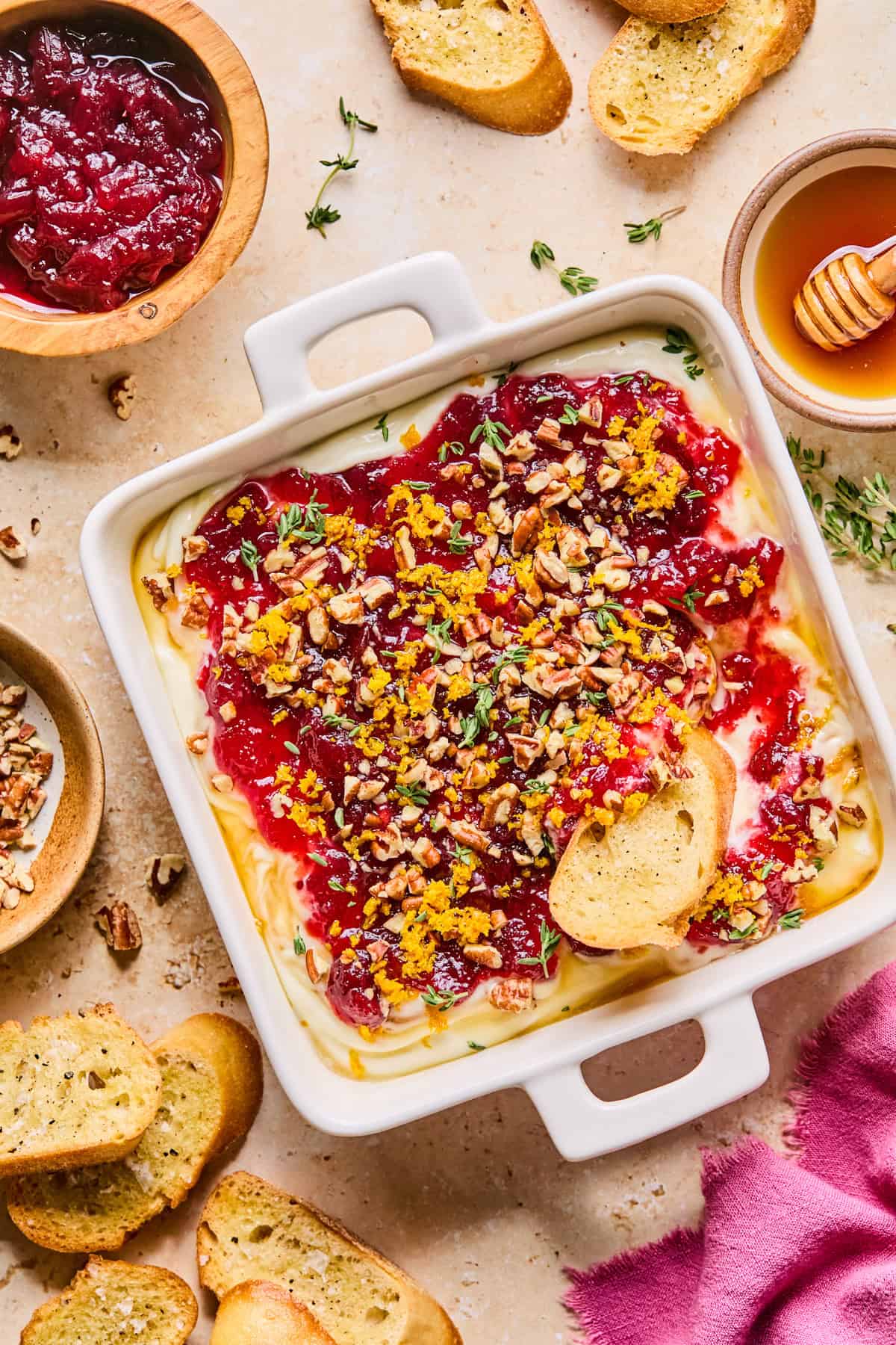 Whipped ricotta dip with honey, cranberry sauce, pecans and other garnish in dish with bread.