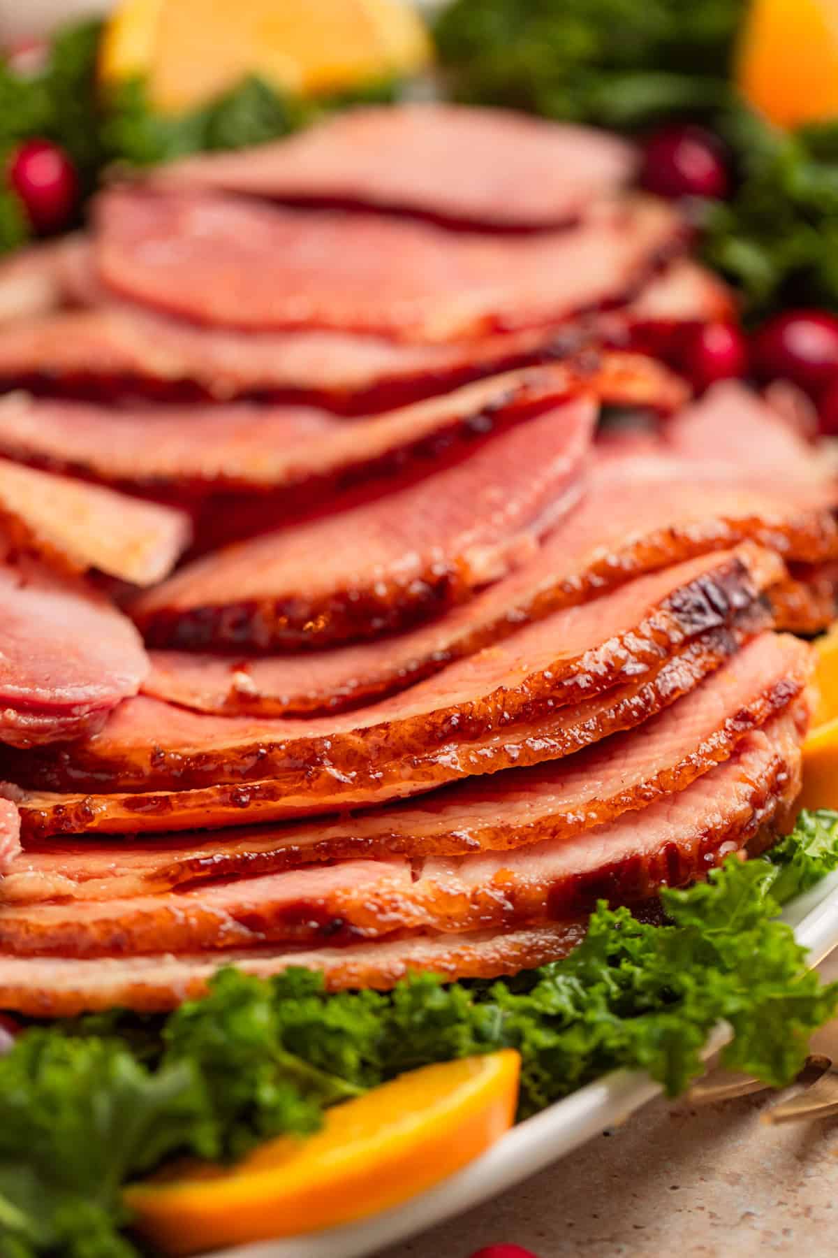 Sliced apricot glazed ham on plate with greens.