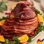 Apricot glazed ham on serving platter with orange slices and cranberries.
