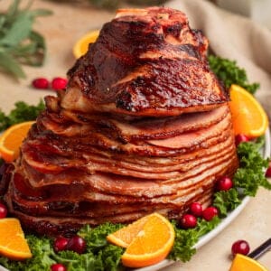 Apricot glazed ham on serving platter with orange slices and cranberries.