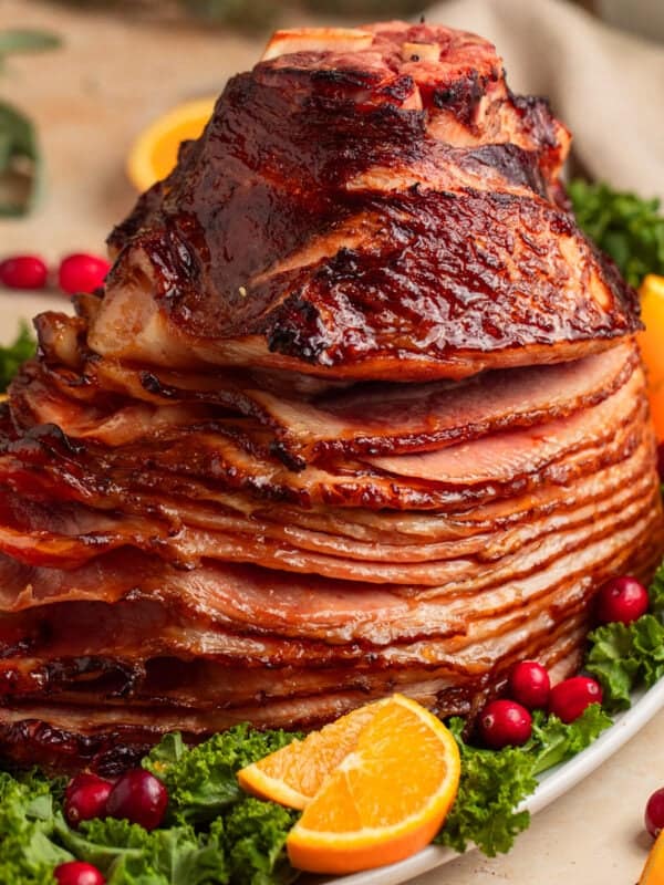 Apricot glazed ham on serving platter with orange slices and cranberries.