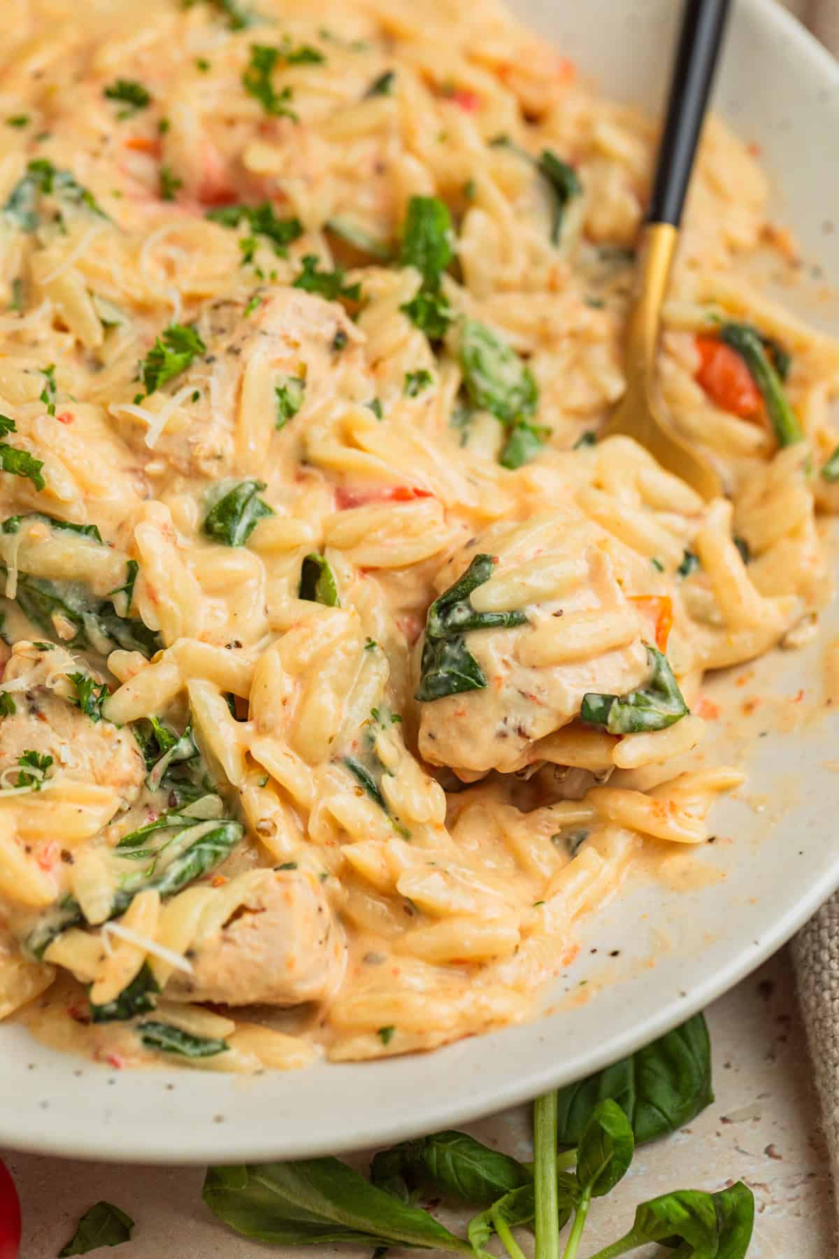 Forkful of orzo with chicken and spinach on plate.