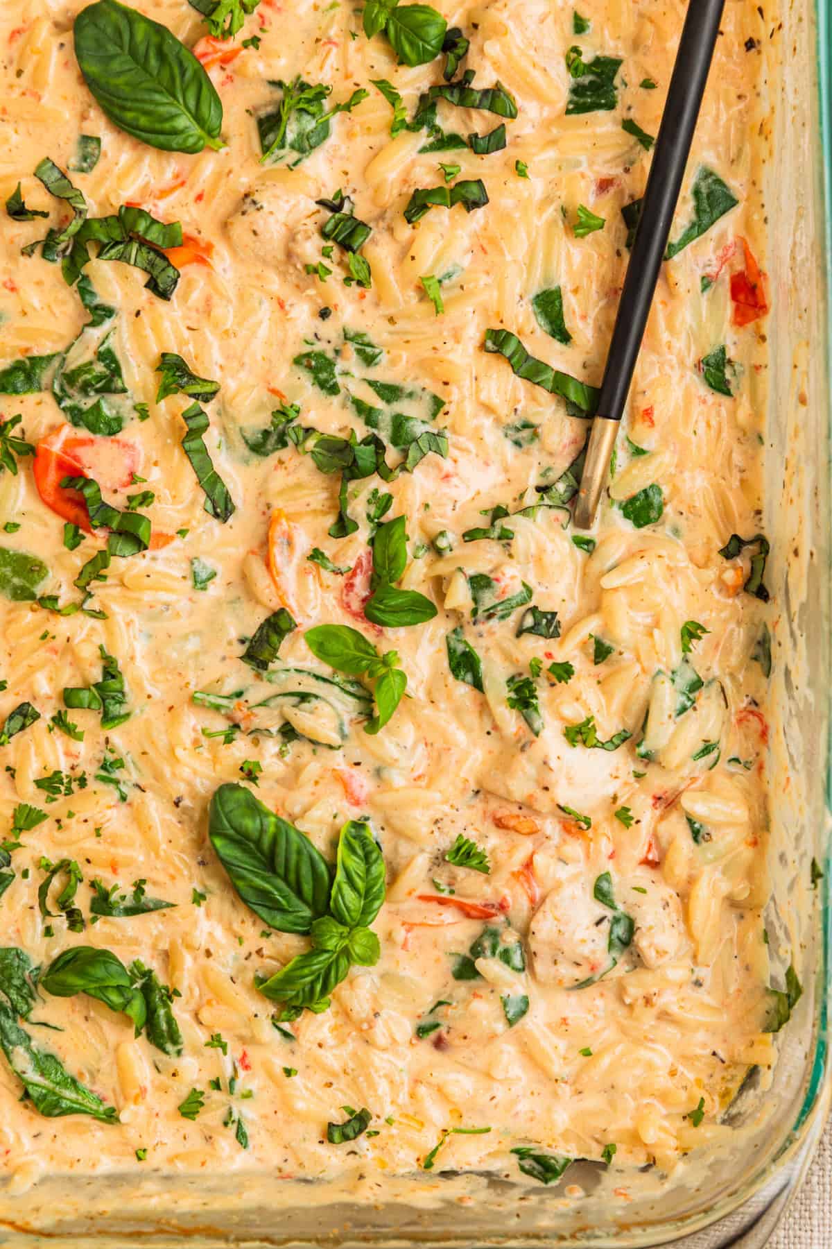 Pan with baked chicken and orzo with basil leaves over top.
