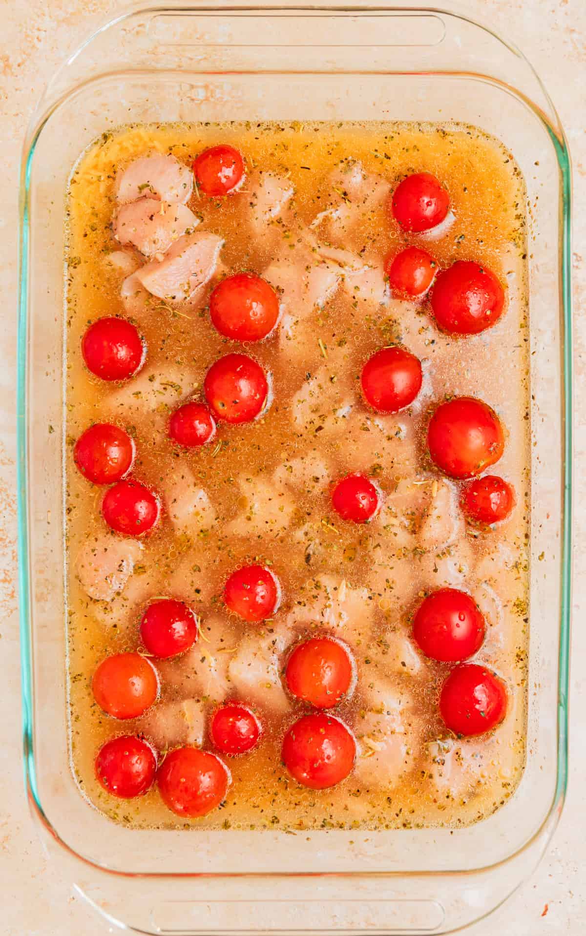Broth, orzo and tomatoes added to baking pan with chicken.