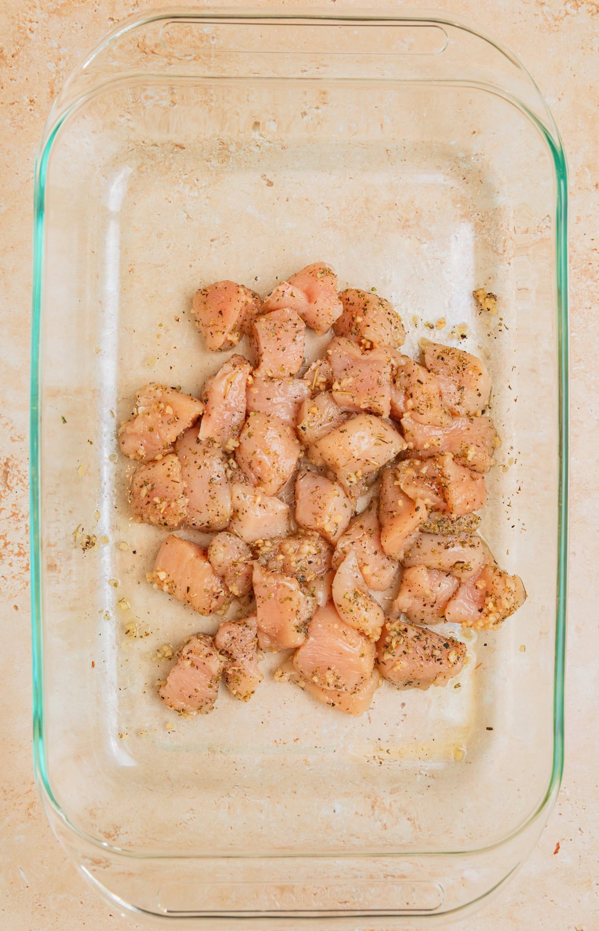 Cubed chicken breast in pan tossed with olive oil and seasoning.