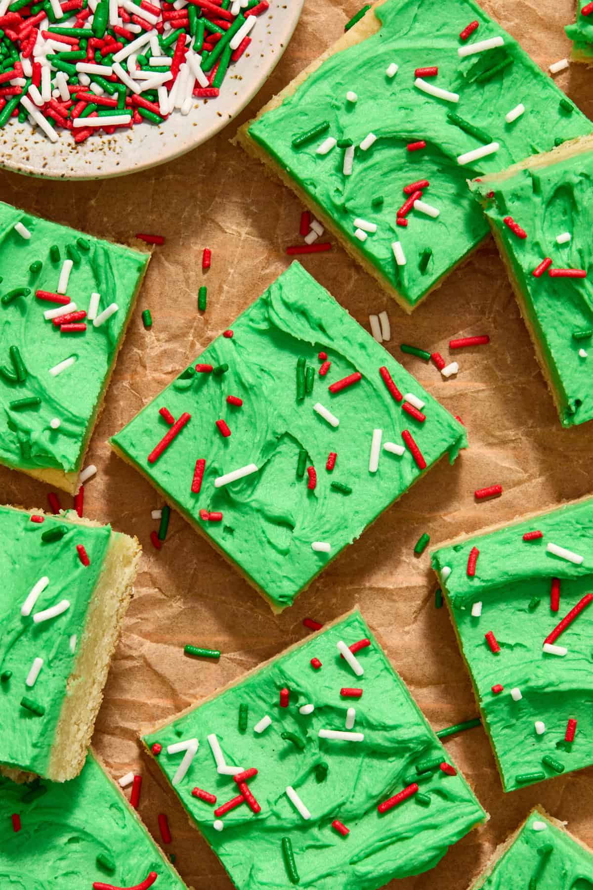 Sugar cookie bars on parchment with green frosting and Christmas color sprinkles.