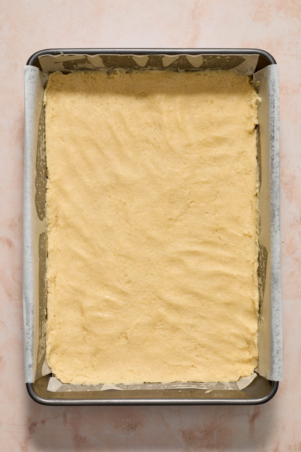 Baking pan with parchment and cookie bar dough pressed in.