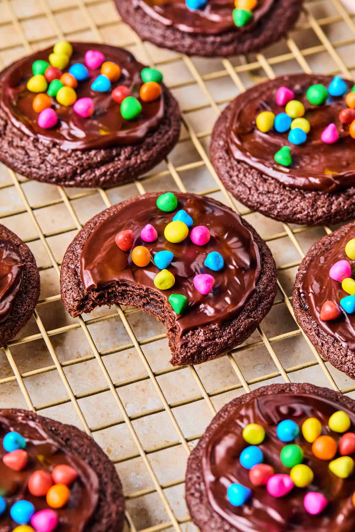 Chocolate cookies with ganache and rainbow chips on top on wire rack.