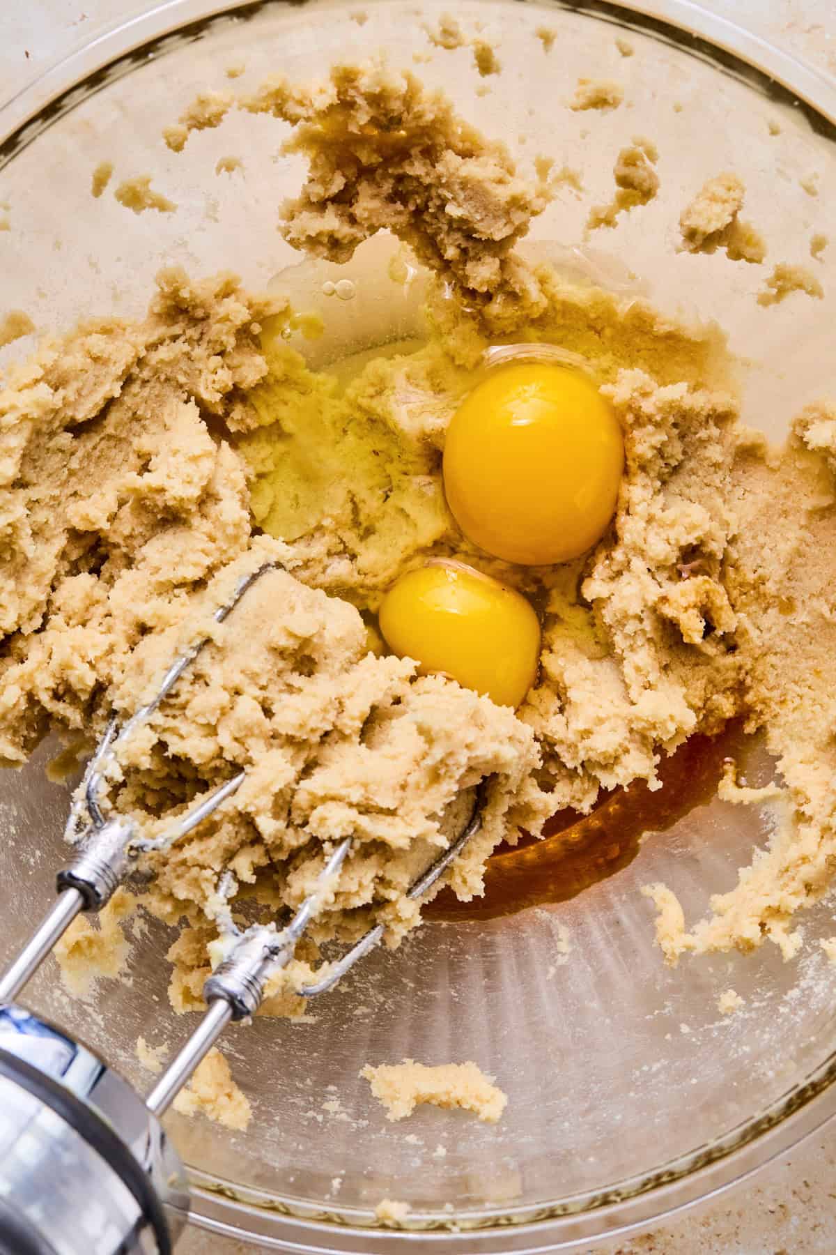 Electric beater propped in bowl with creamed butter and sugar with eggs added.