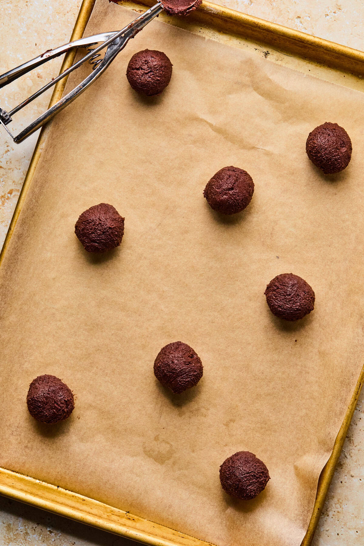 Parchment lined cookie sheet with chocolate cookie dough balls.