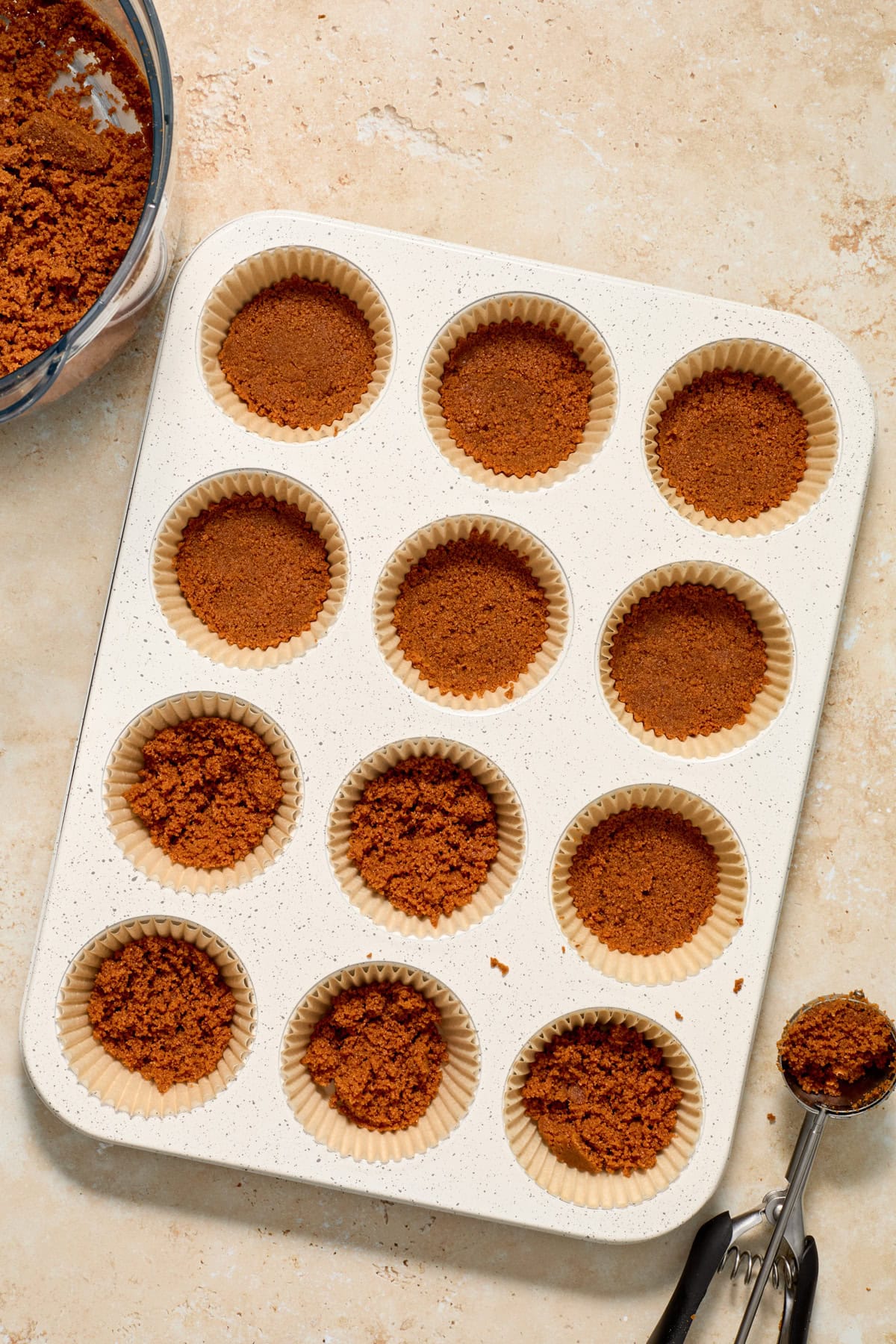 Biscoff cookie crust being pressed into muffin tin.
