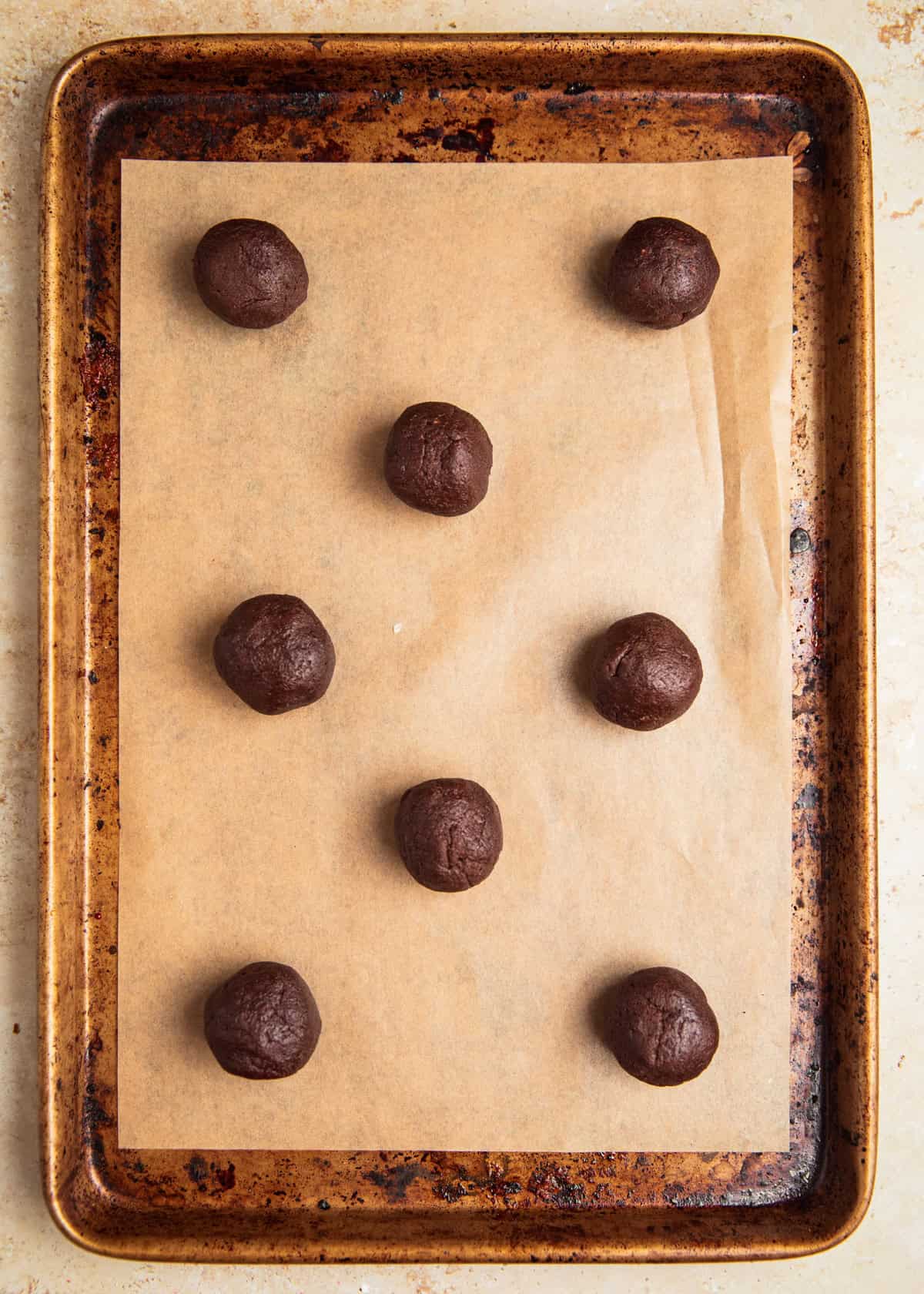 Rolled chocolate cookie dough balls on parchment lined cookie sheet.