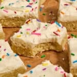 Vanilla bean frosted sugar cookie bars with rainbow sprinkles on parchment.