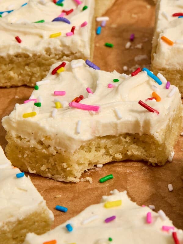 Vanilla bean frosted sugar cookie bars with rainbow sprinkles on parchment.