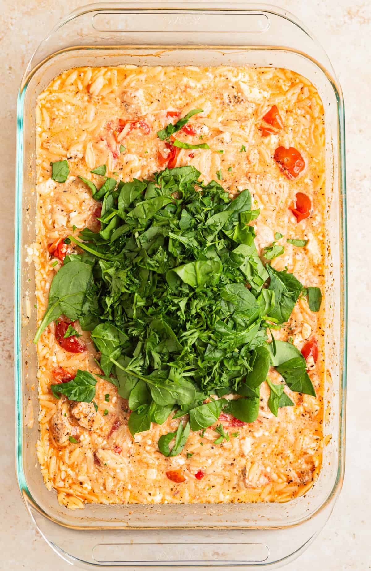 Chopped spinach and parsley on top of pan with chicken orzo bake.