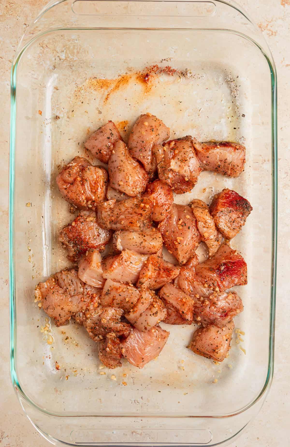 Chicken pieces in pan tossed in olive oil and seasonings.