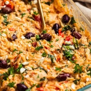 Creamy feta baked chicken and orzo topped with olives, parsley and basil in pan.