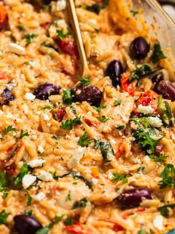 Creamy feta baked chicken and orzo topped with olives, parsley and basil in pan.