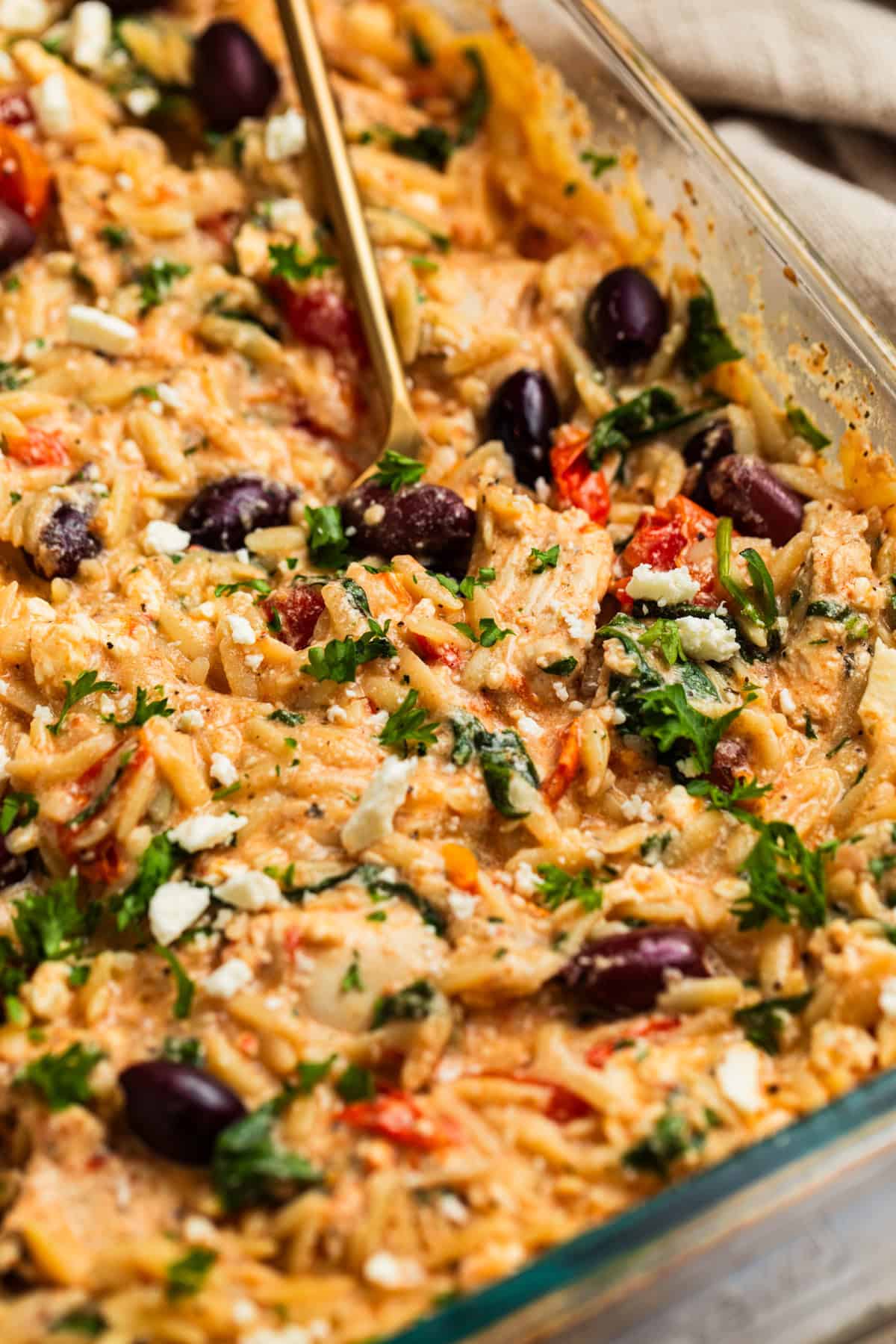 Greek chicken and orzo in glass pan with spoon scooping into it.
