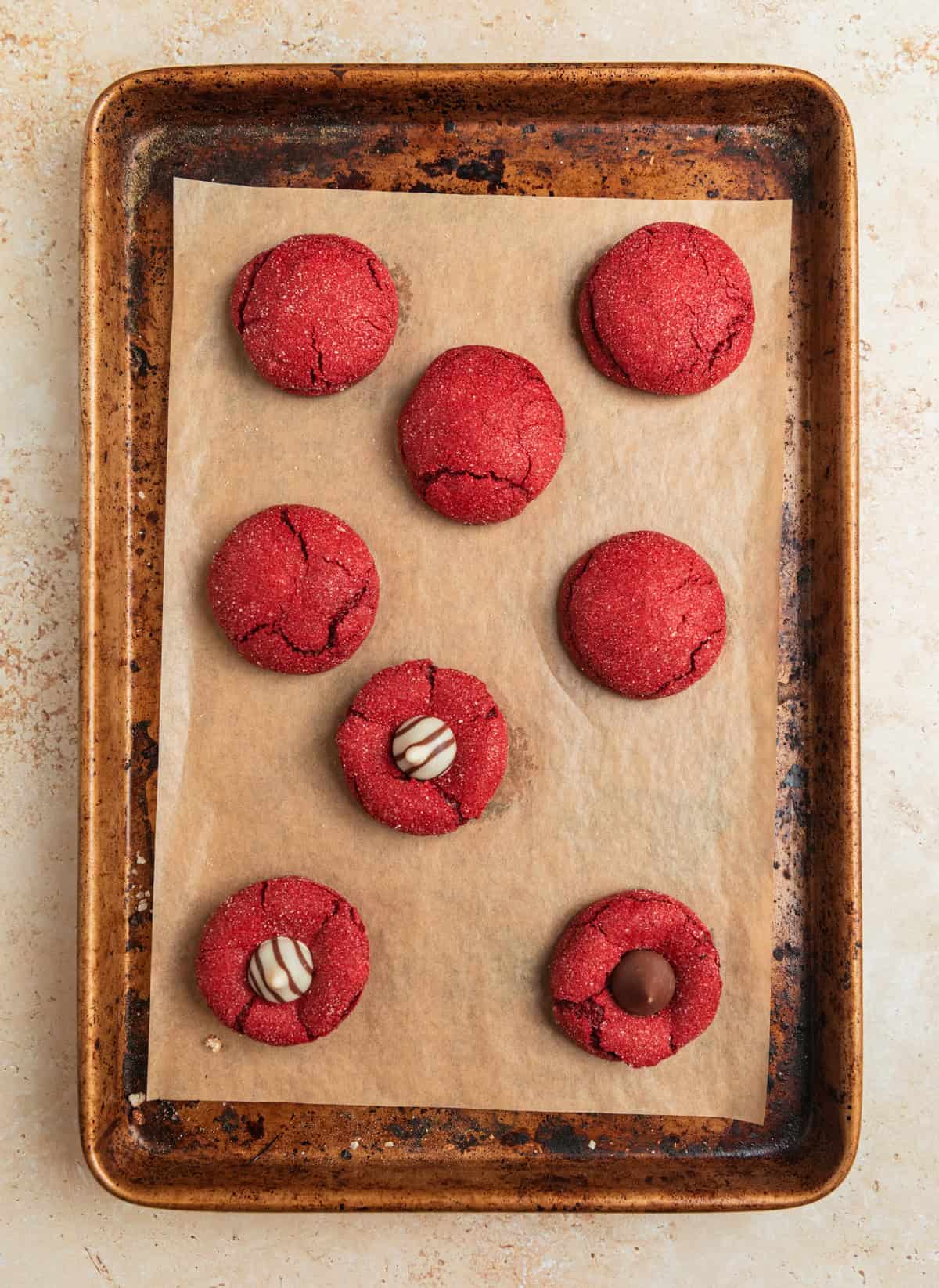 Baked red velvet cookies on pan with Hershey Kiss and Hugs pressed into some of the cookies.