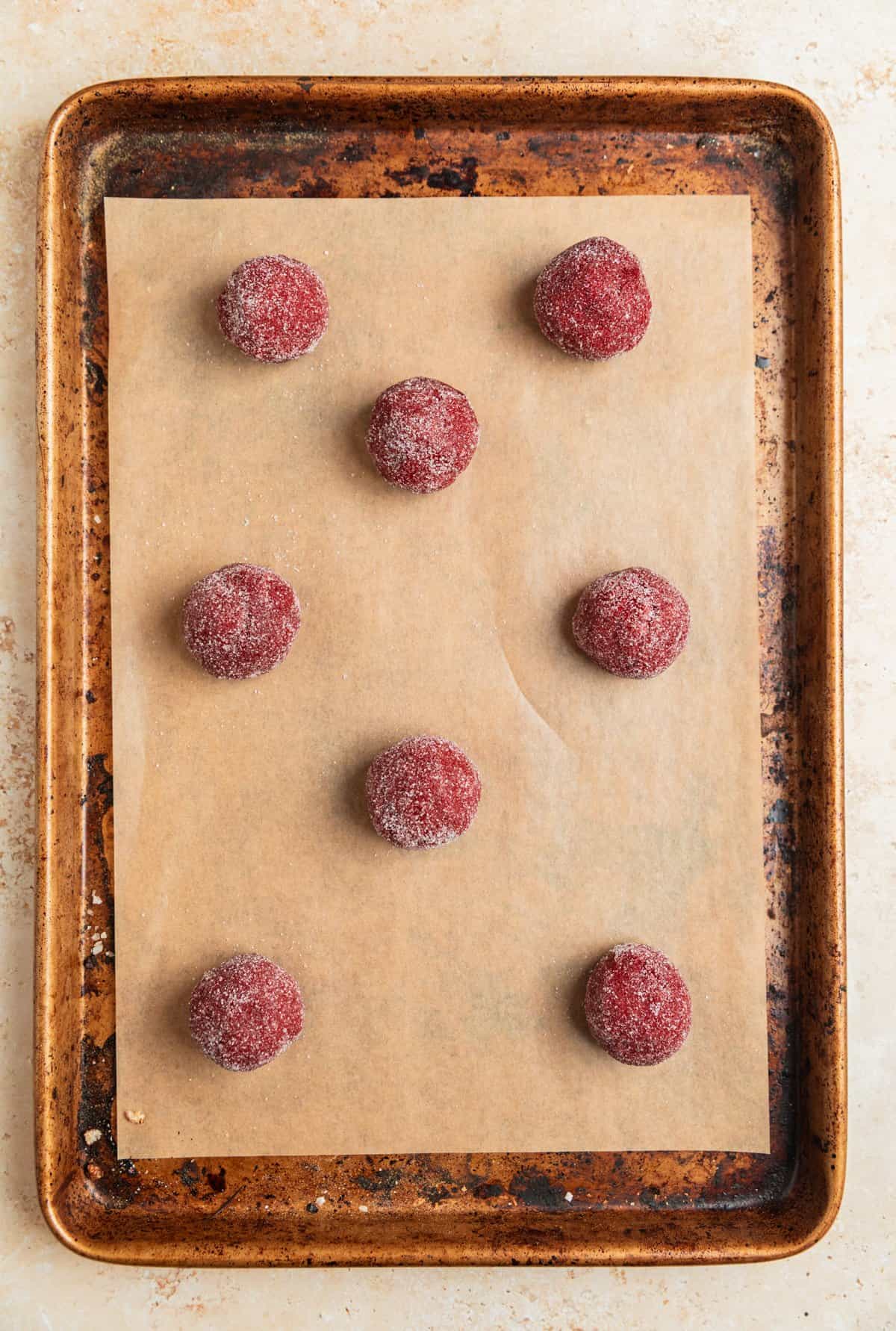 Red velvet cake mix cookie dough balls rolled in sugar on cookie sheet.