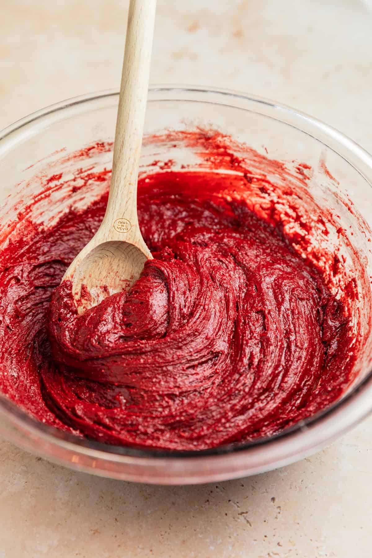 Red velvet cake mix cookie dough in bowl with wooden spoon.
