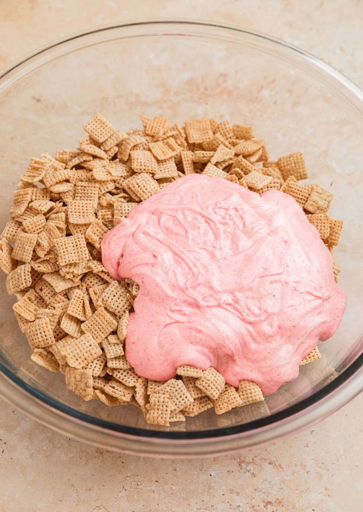 Melted strawberry white chocolate poured over rice Chex in mixing bowl.