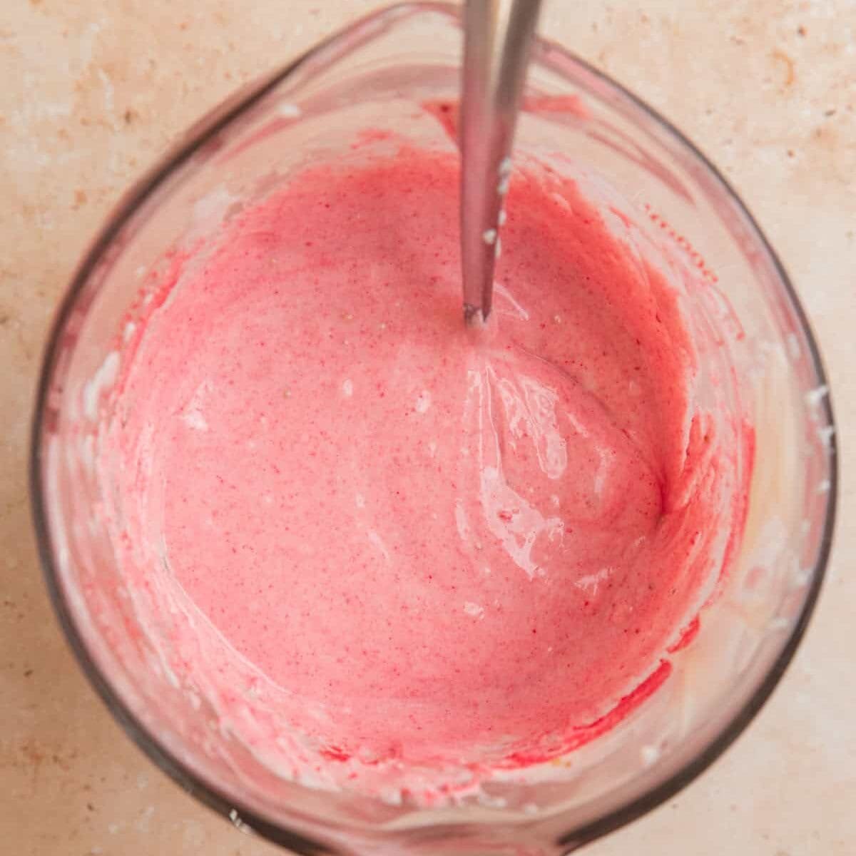 Pink melted white chocolate mixture in glass with spoon.