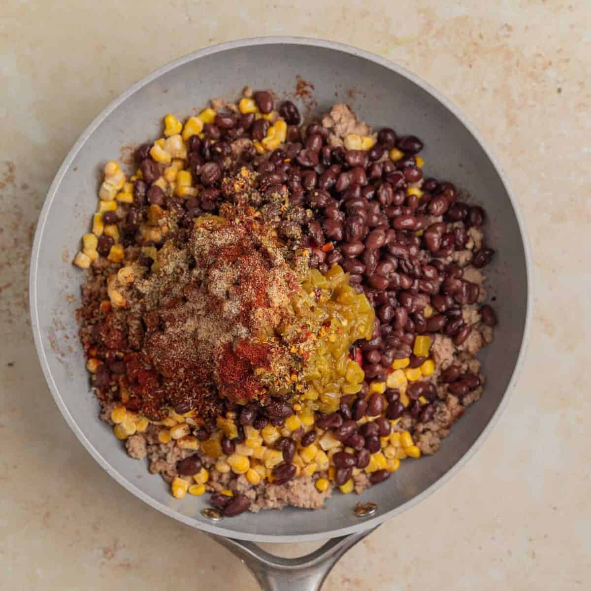 Meat in skillet with diced tomatoes, beans, corn and other ingredients added.