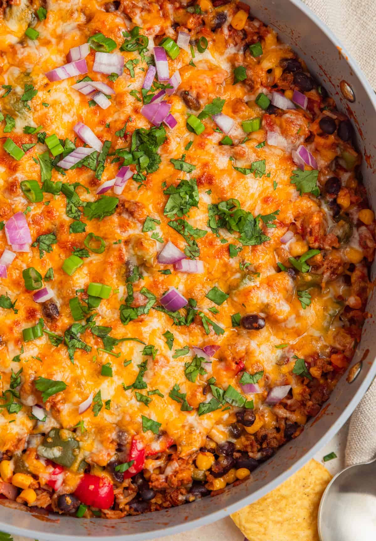 Cheesy taco rice skillet topped with chopped cilantro, green onions and red onions.