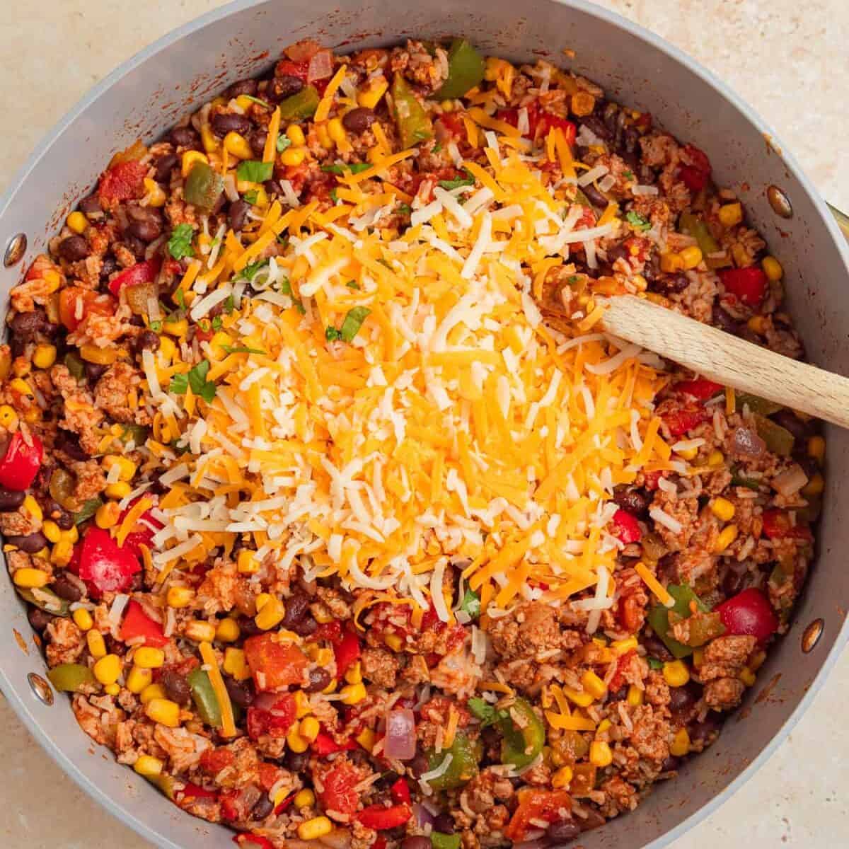 Shredded cheese added to skillet with turkey rice taco ingredients.