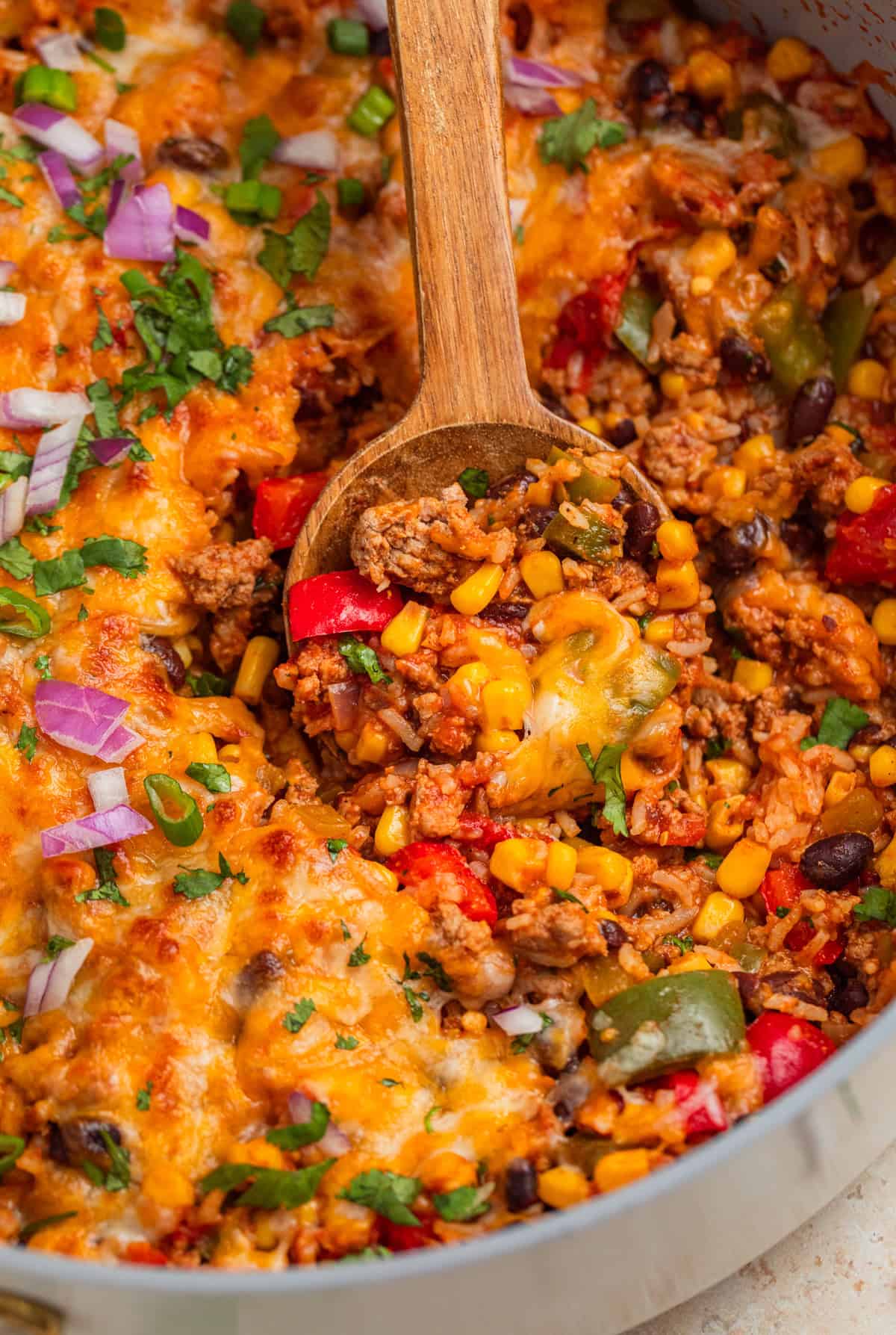 Wood spoon scooping into skillet with turkey and rice mixture topped with melted cheese.