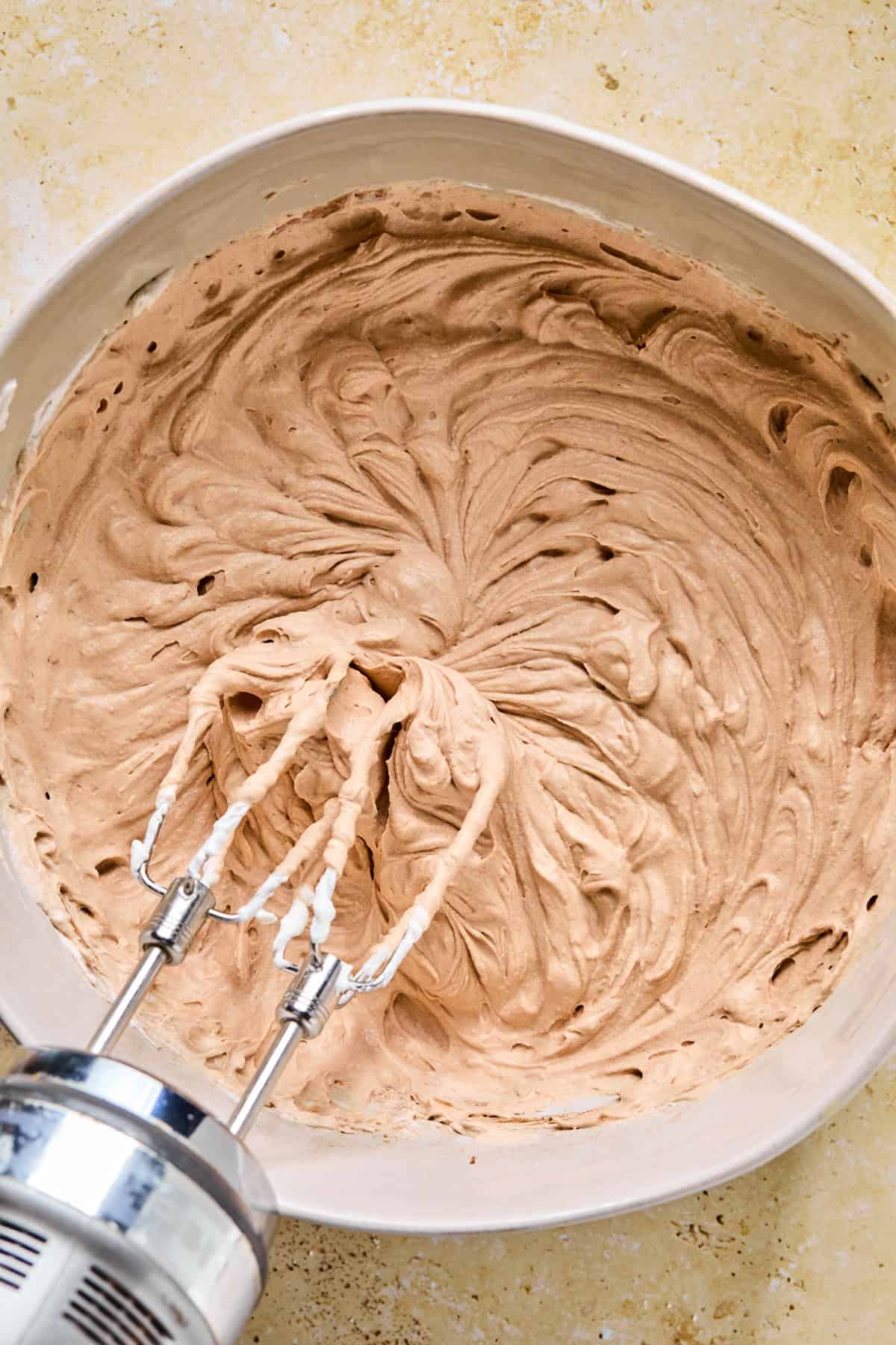 Chocolate whipped cream mixture in bowl with electric mixer propped above.