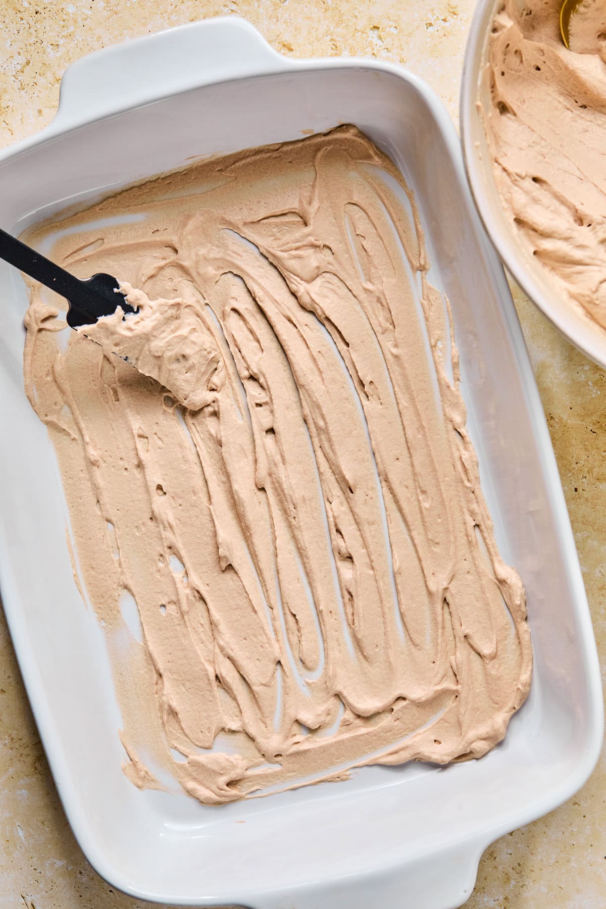Chocolate whipped cream mixture spread in layer in pan with spatula.