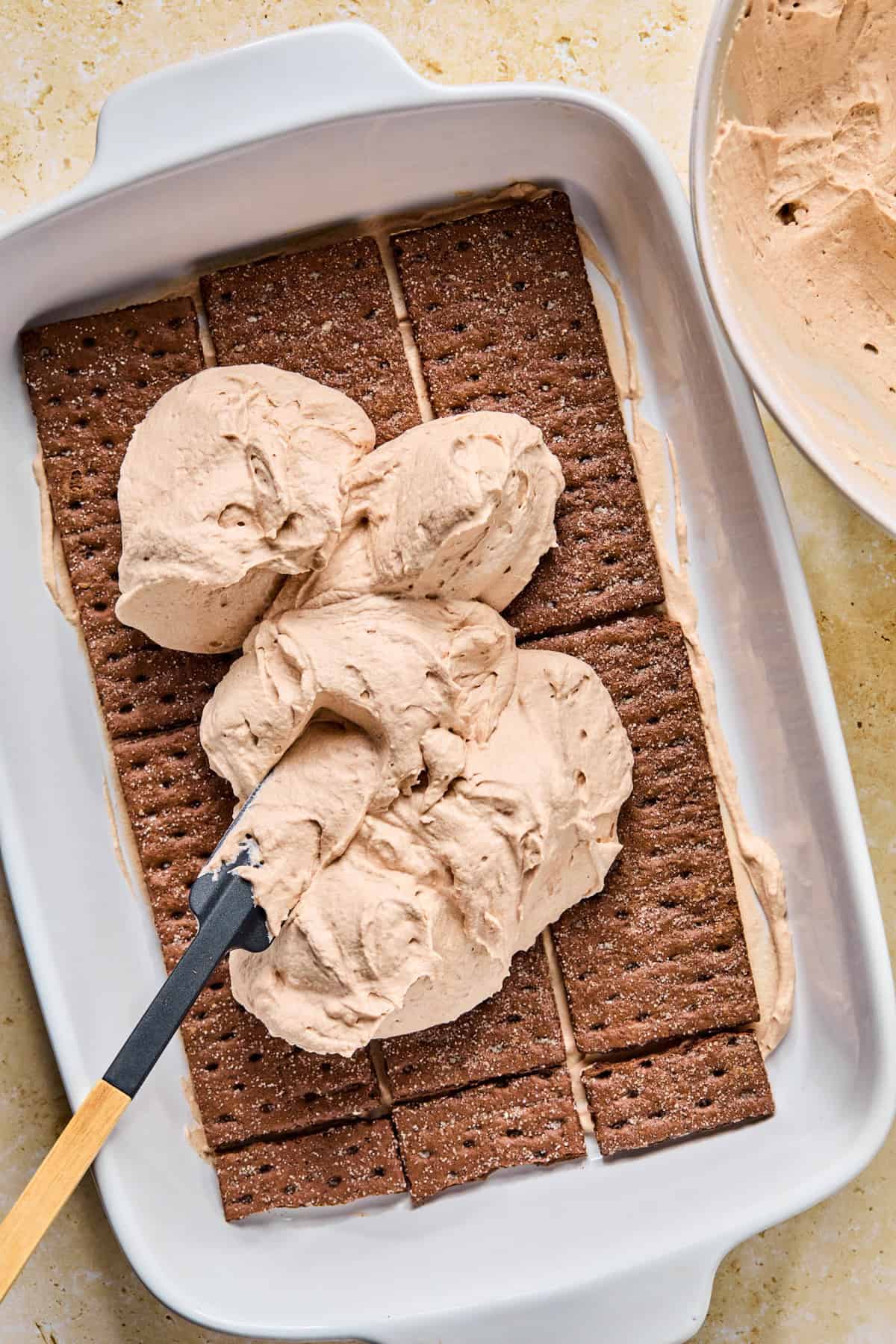Dollops of chocolate cream mixture over top of chocolate graham layer for icebox cake.