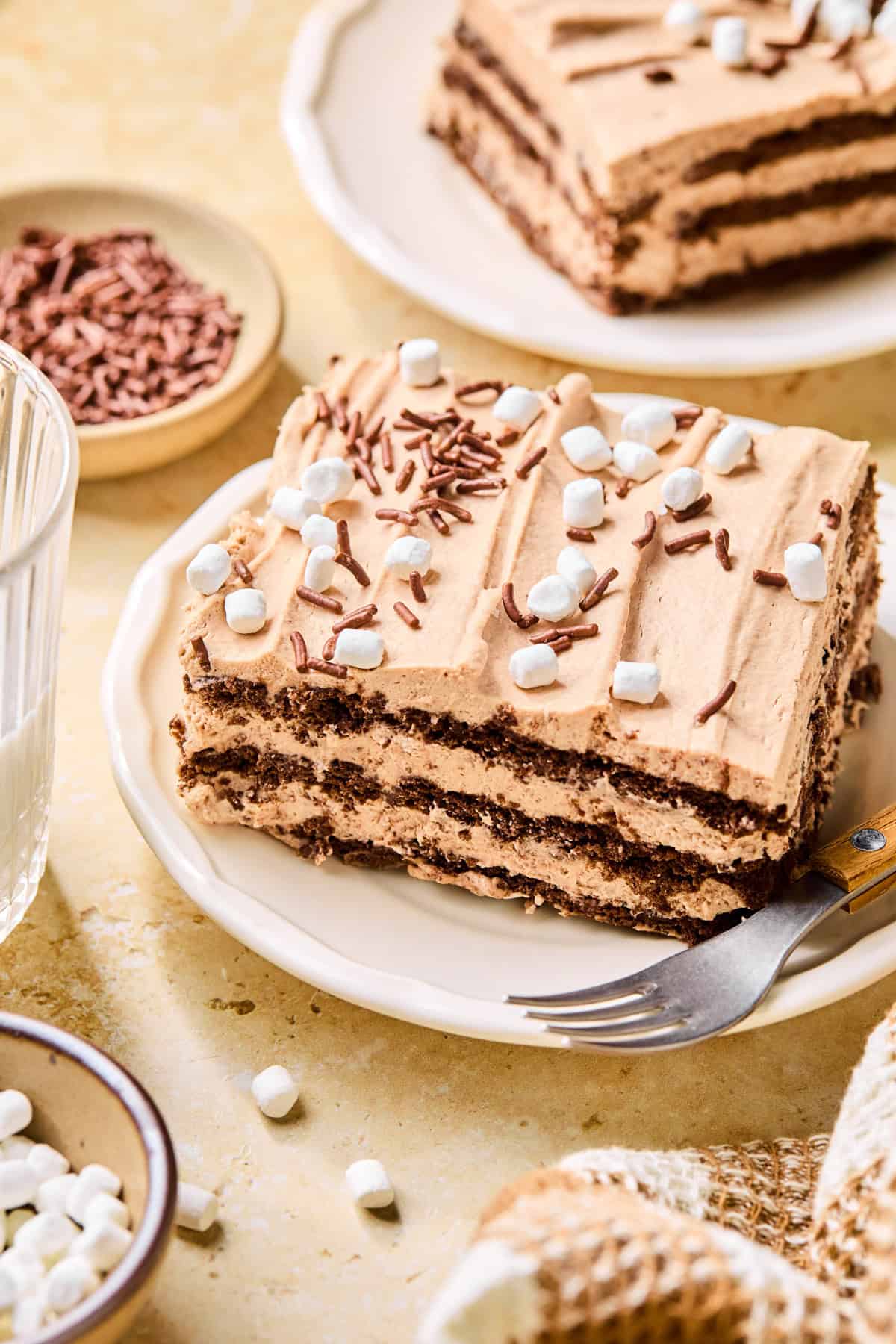 Hot chocolate icebox cake slice on plate with fork topped with chocolate sprinkles and marshmallows.