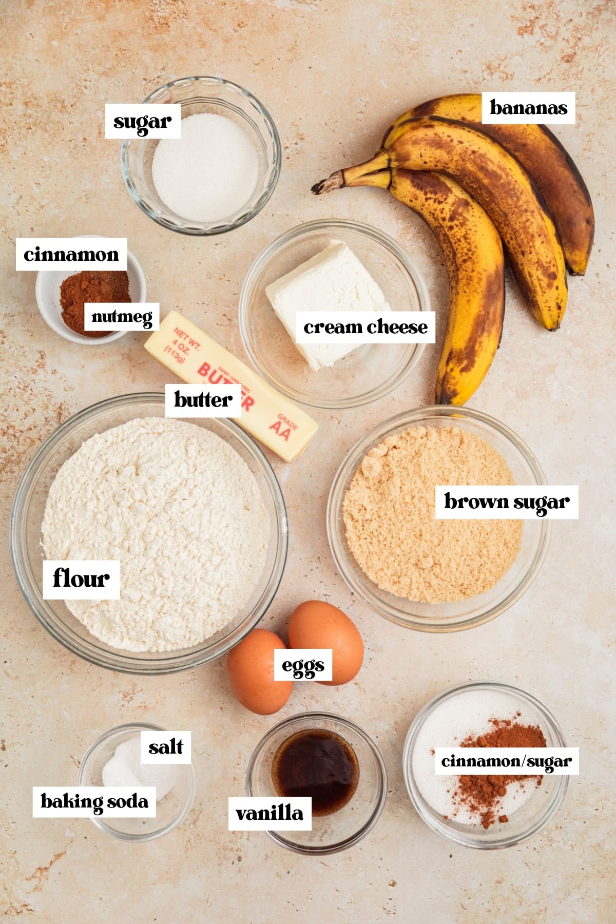 Brown bananas, flour, butter, sugar and other labeled ingredients on surface.
