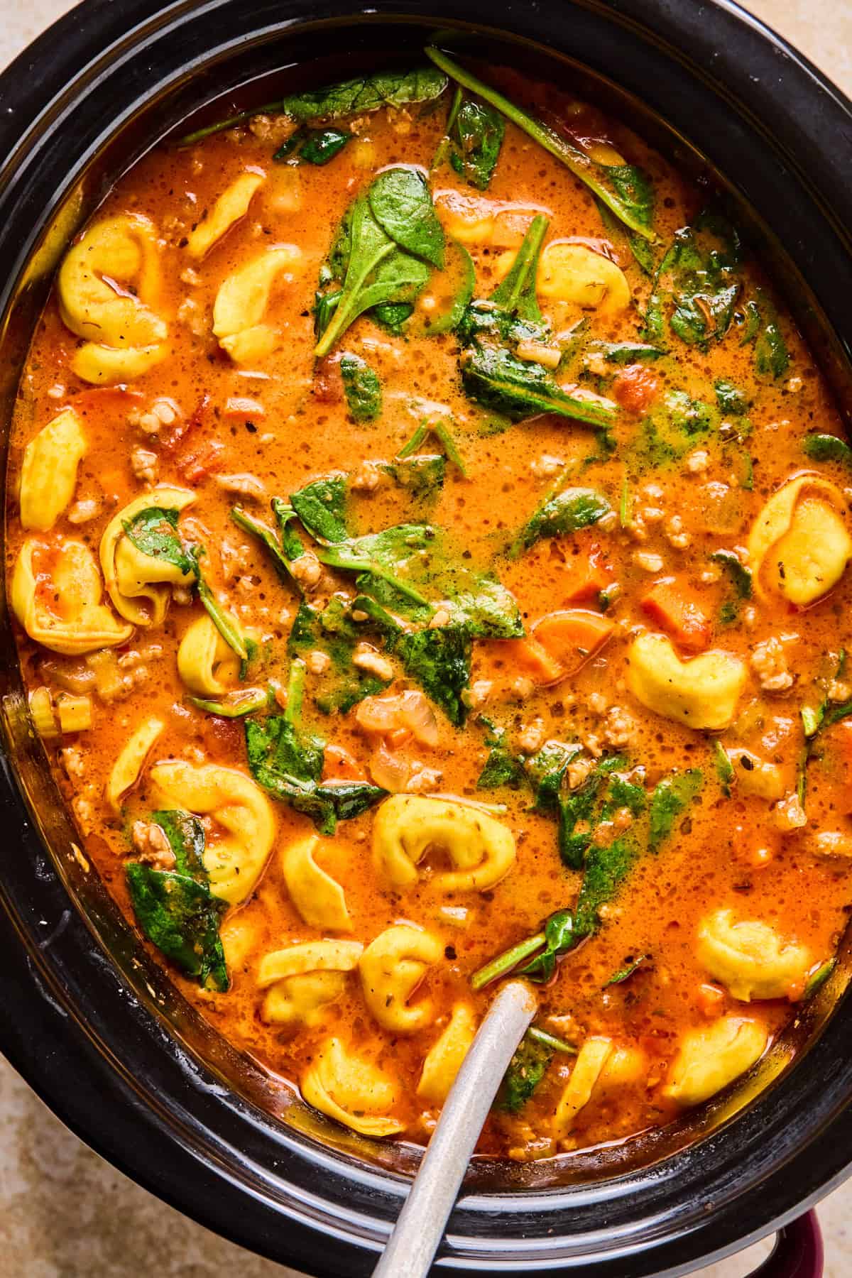 Sausage tortellini soup in slow cooker with ladle.