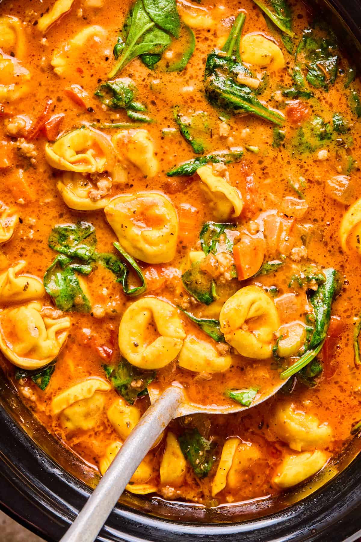 Crockpot with tomato based soup with sausage and tortellini and ladle spooning soup.