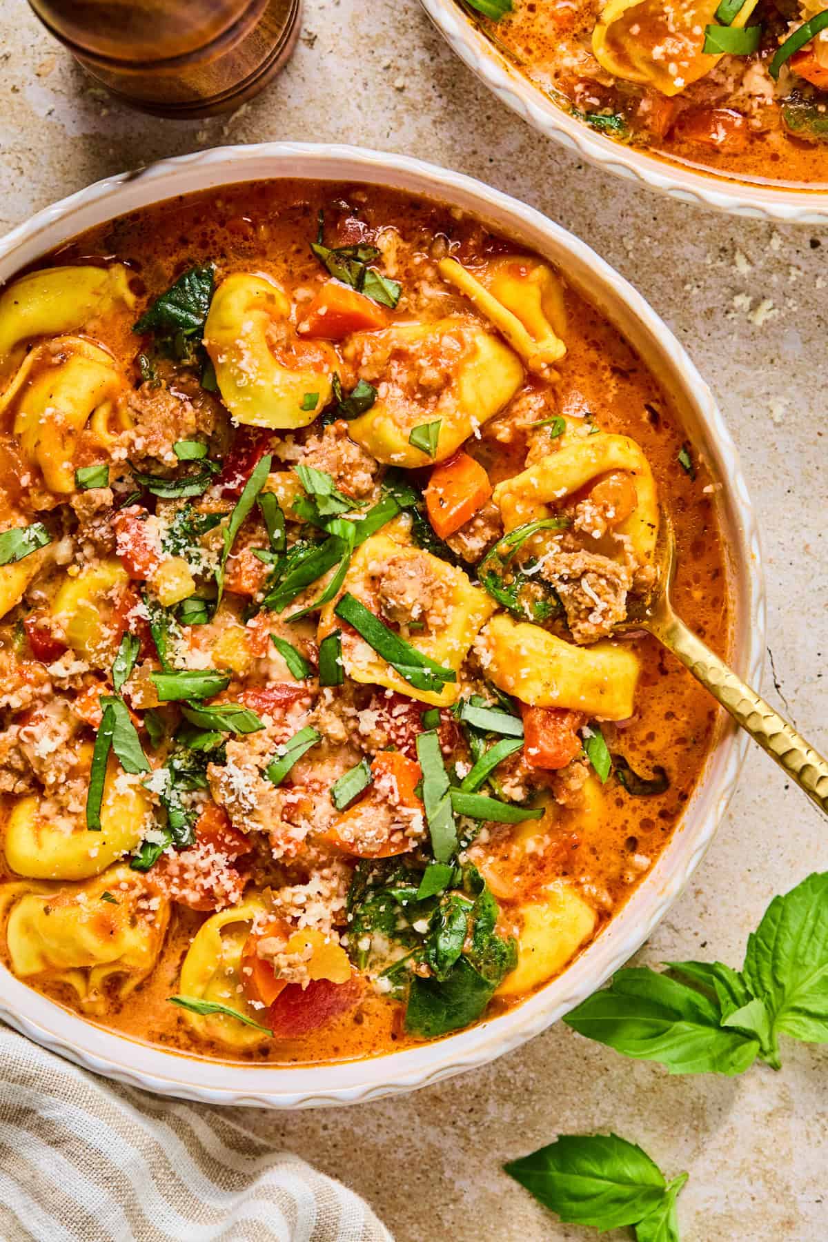 Bowl with sausage tortellini soup topped with fresh basil.